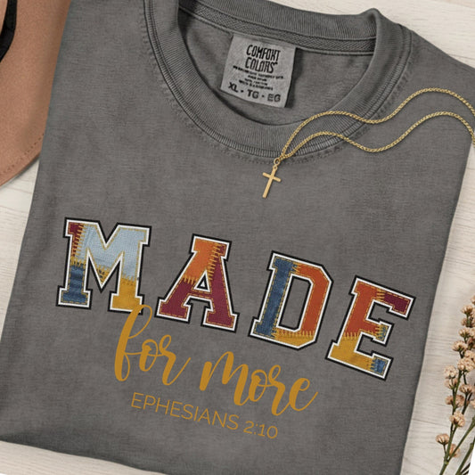 Flatlay of a Comfort Colors 1717 pepper “Made for More” Ephesians 2:10 t-shirt with colorful varsity-style letters and gold script accent. A stylish women’s scripture tee - faith-based apparel for women and modern Christian shirt, perfect Christian mom gift idea reminding her of God’s calling.