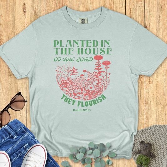 Bay Green Comfort Colors 1717 tshirt displaying a floral botanical graphic and Bible verse. Soft green Christian women tee with the text "They Flourish," styled for US faith wear collections.
