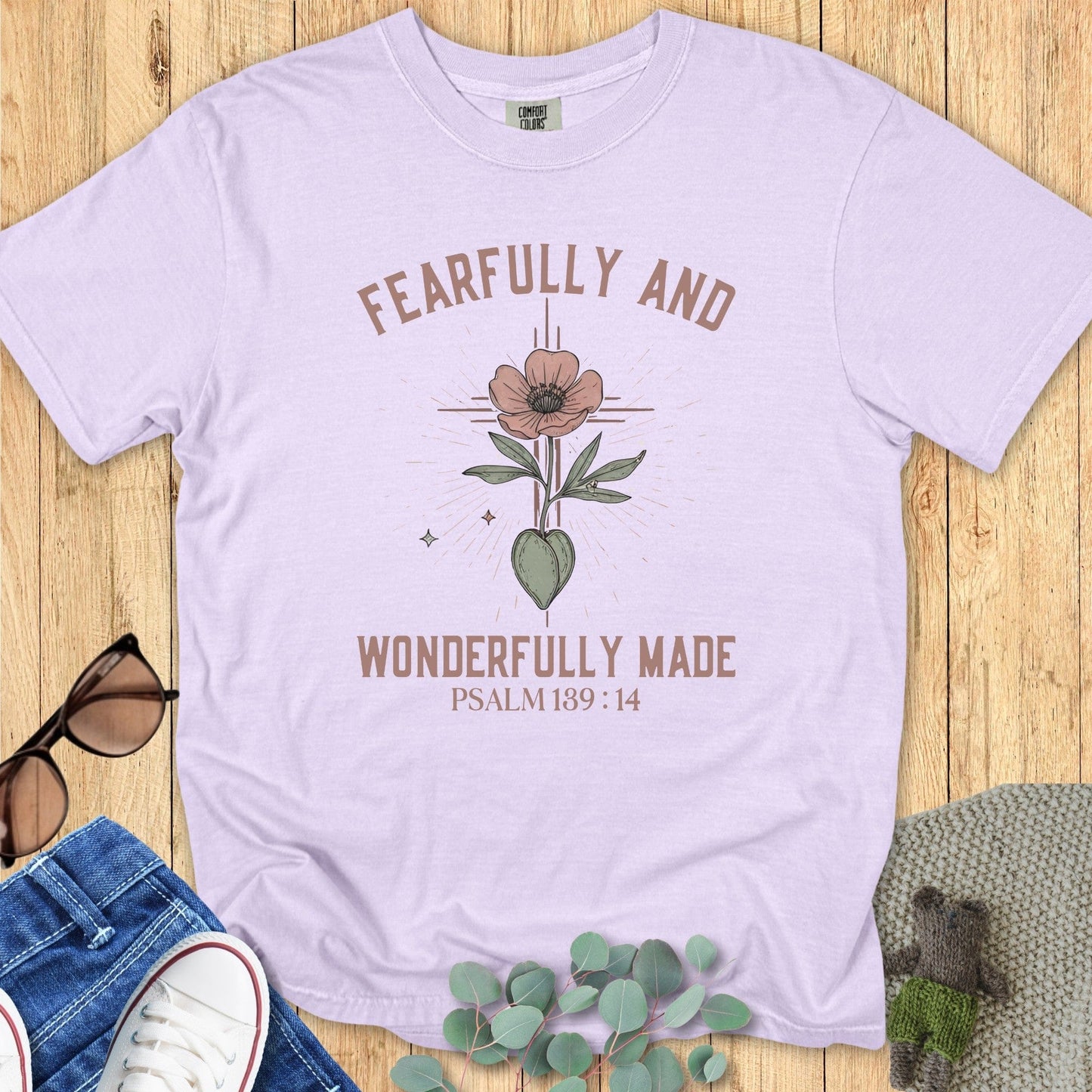Flatlay of a Comfort Colors 1717 orchid “Fearfully and Wonderfully Made – Psalm 139:14” t-shirt featuring a hand-drawn floral design. A lovely and uplifting faith-based apparel for women piece, ideal for Christian mom gift ideas.