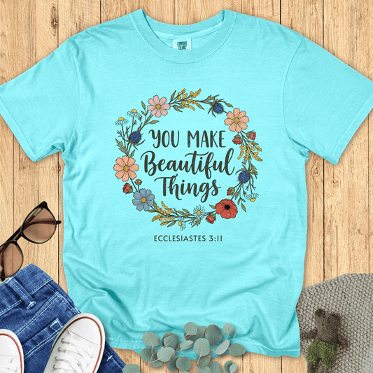 Flat lay of a chalky mint Comfort Colors Christian t-shirt with a floral wreath design and the words “You Make Beautiful Things” from Ecclesiastes 3:11. Styled with jeans, white sneakers, and accessories for a boutique aesthetic.