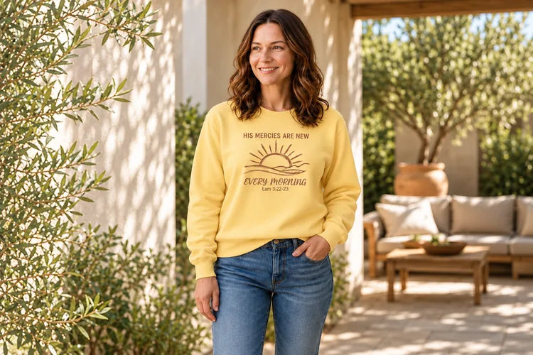 Woman wearing the Butter His Mercies Are New Every Morning sweatshirt on a sunlit porch