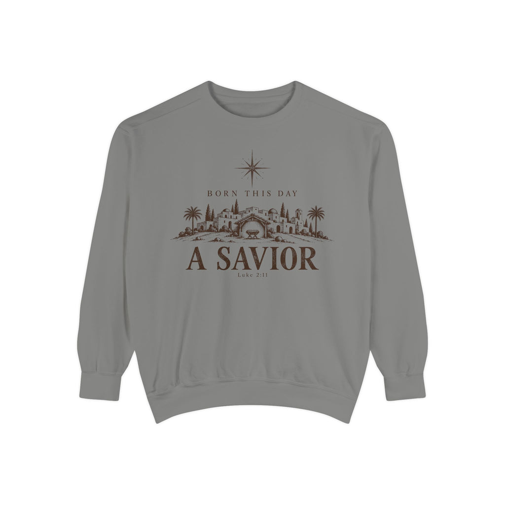 Grey Christian Christmas sweatshirt with Born This Day A Savior lettering, a star over a Bethlehem town scene, a manger and Luke 2:11.