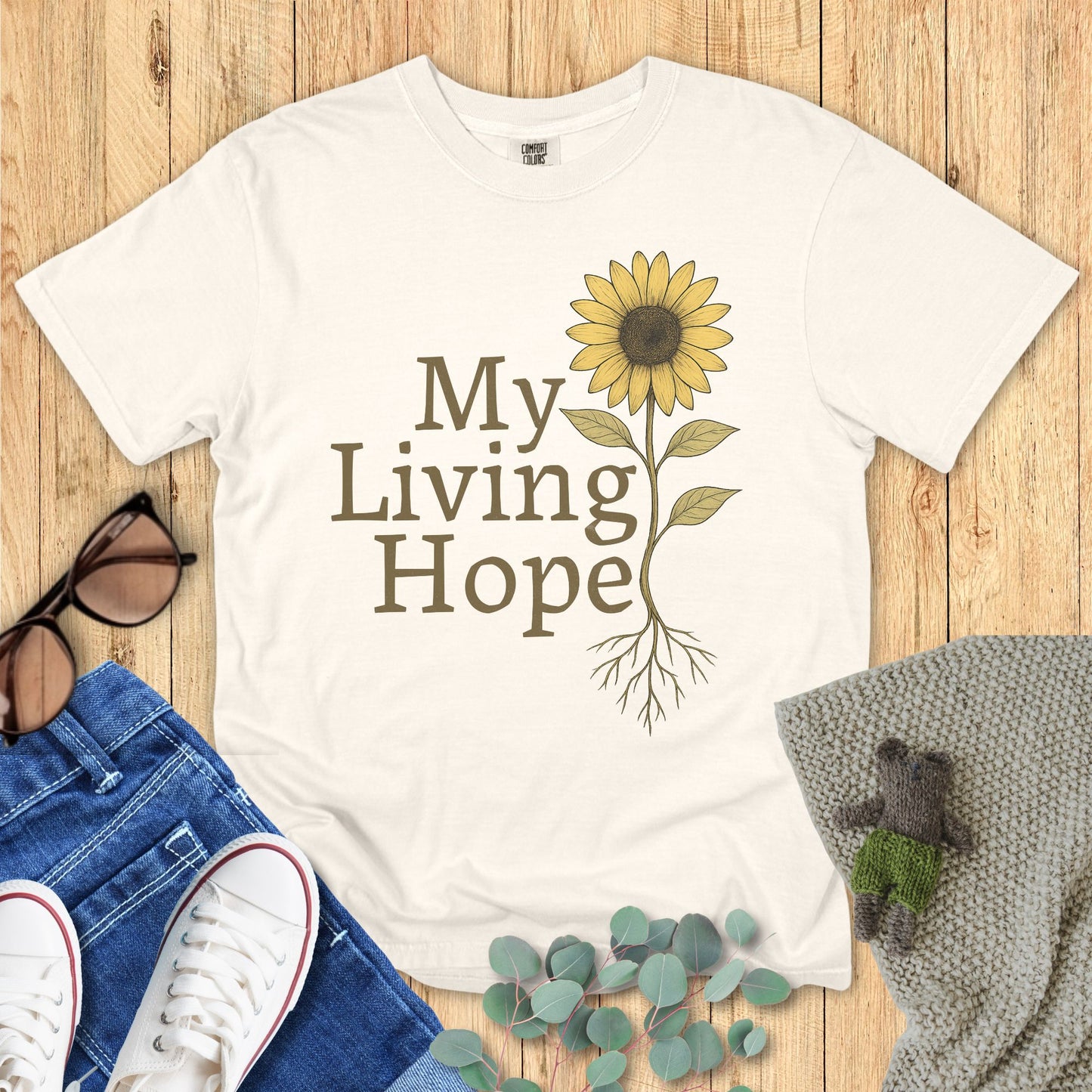Ivory White t-shirt with sunflower design and 'My Living Hope' text on a wooden surface with accessories.