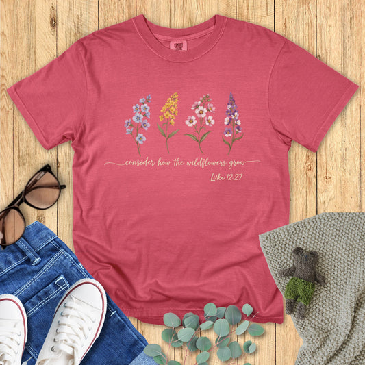 Red t-shirt with floral design and text on a wooden surface with accessories.