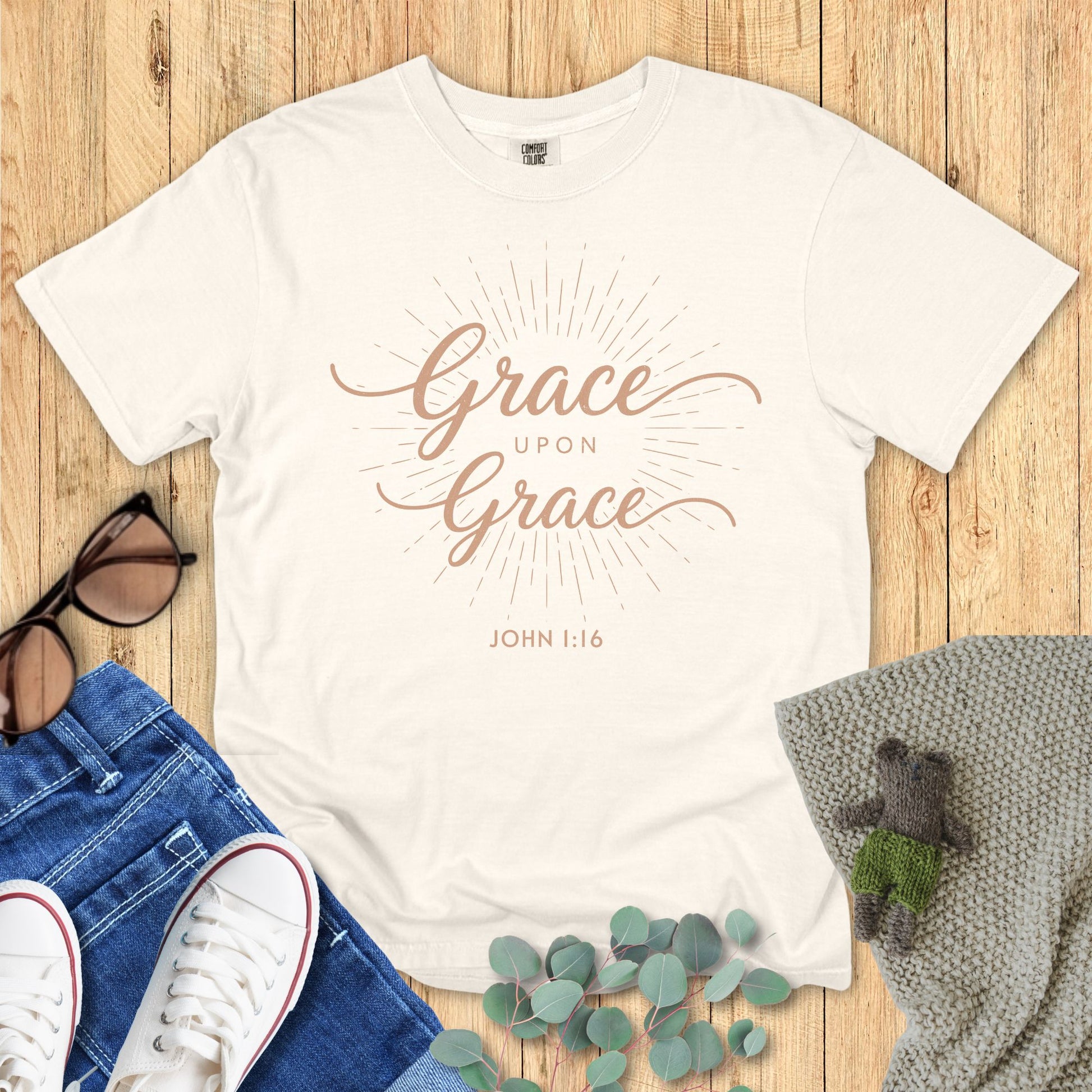 Ivory White t-shirt with 'Grace upon Grace' text on a wooden surface with accessories.