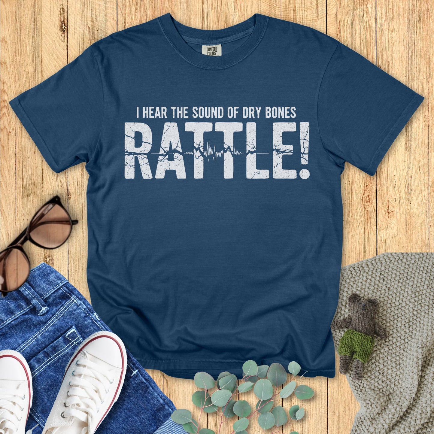 Blue t-shirt with text on a wooden surface with accessories.