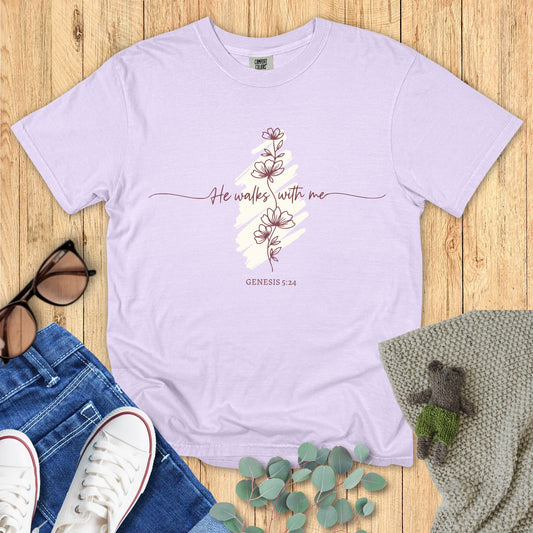 Lavender t-shirt with floral design and text on a wooden surface with accessories.