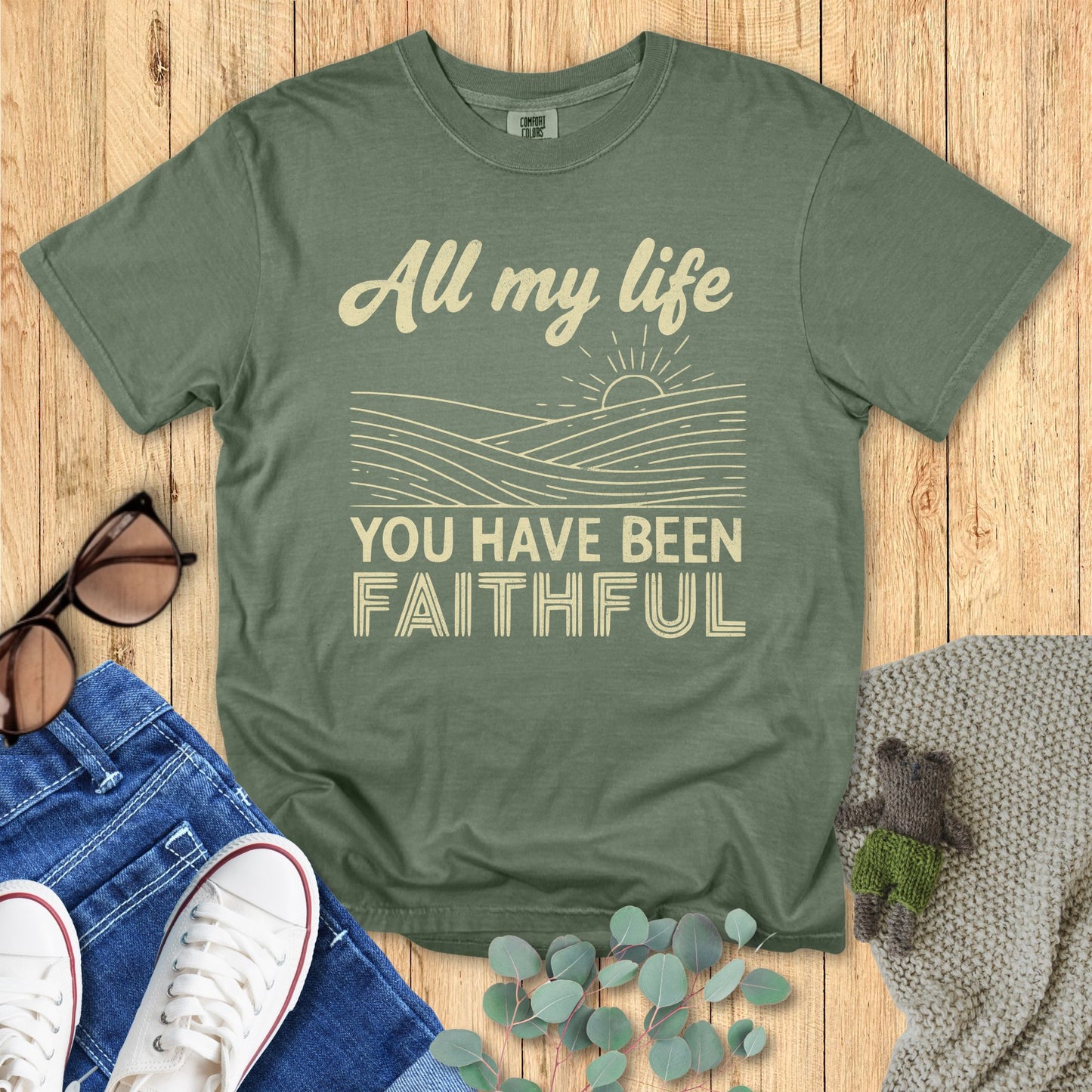 Green t-shirt with motivational quote on a wooden surface with accessories.