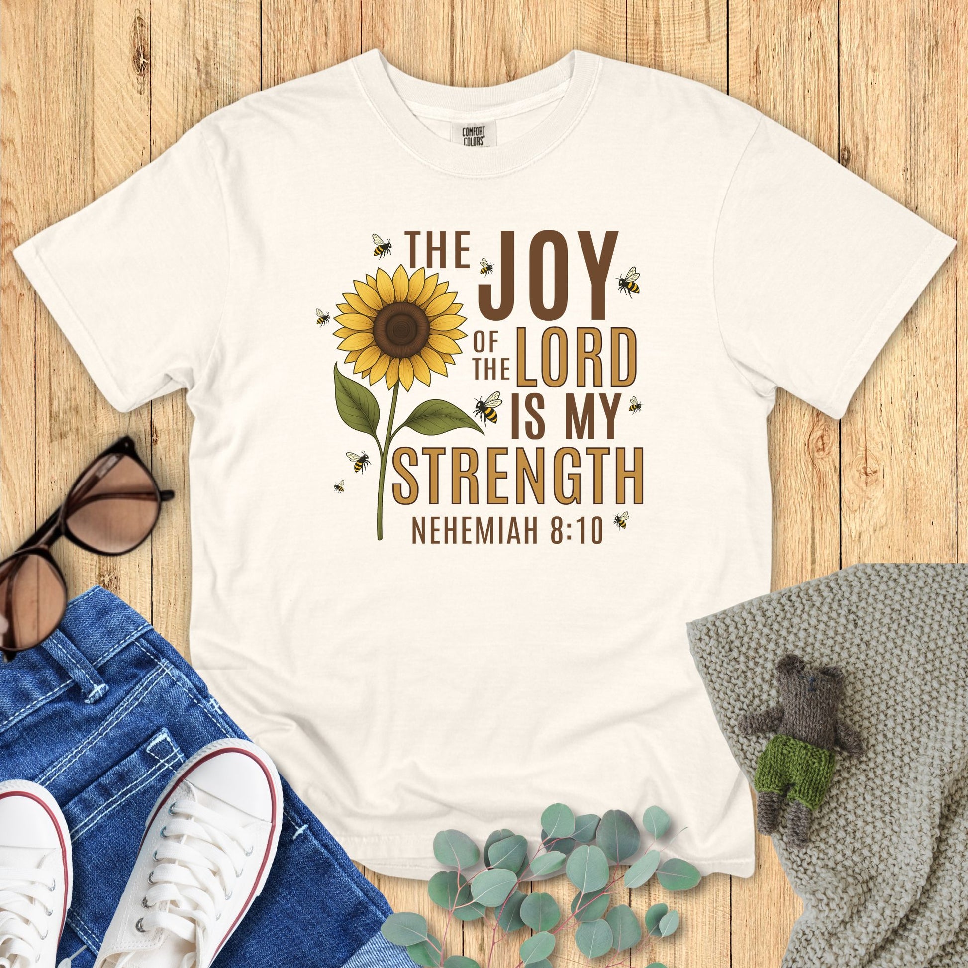 Ivory White t-shirt with sunflower design and text on a wooden surface with accessories.