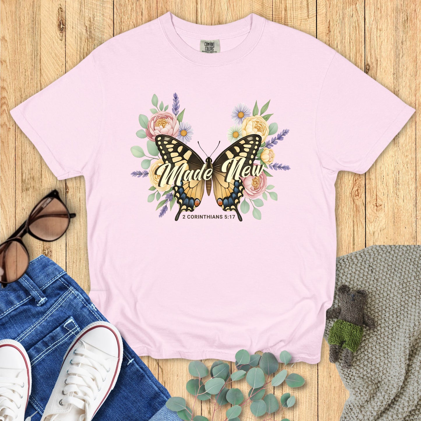 Pink t-shirt with butterfly and floral design on a wooden surface with jeans and sneakers.