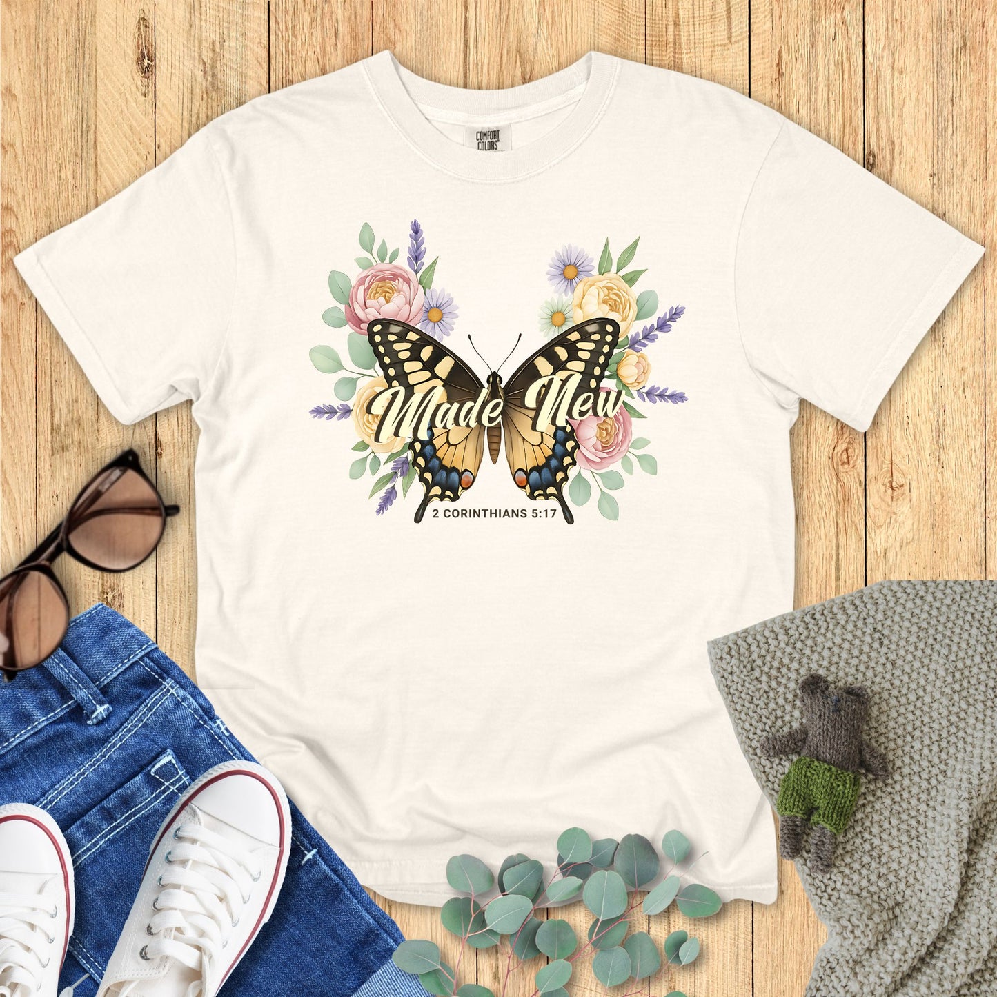 Ivory White t-shirt with butterfly and floral design on a wooden surface with accessories.
