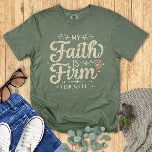 Green t-shirt with 'My Faith Is Firm' text on a wooden surface with accessories.