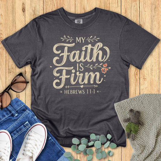 Dark gray t-shirt with 'My Faith Is Firm' text on a wooden surface with accessories.