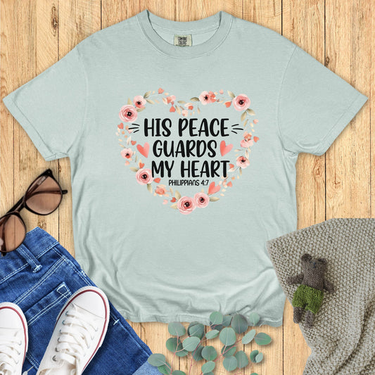 Light blue t-shirt with floral design and text on a wooden surface with accessories.