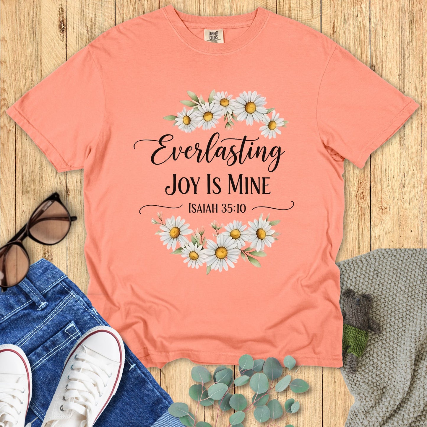 Peach t-shirt with floral design and text on a wooden surface with accessories.