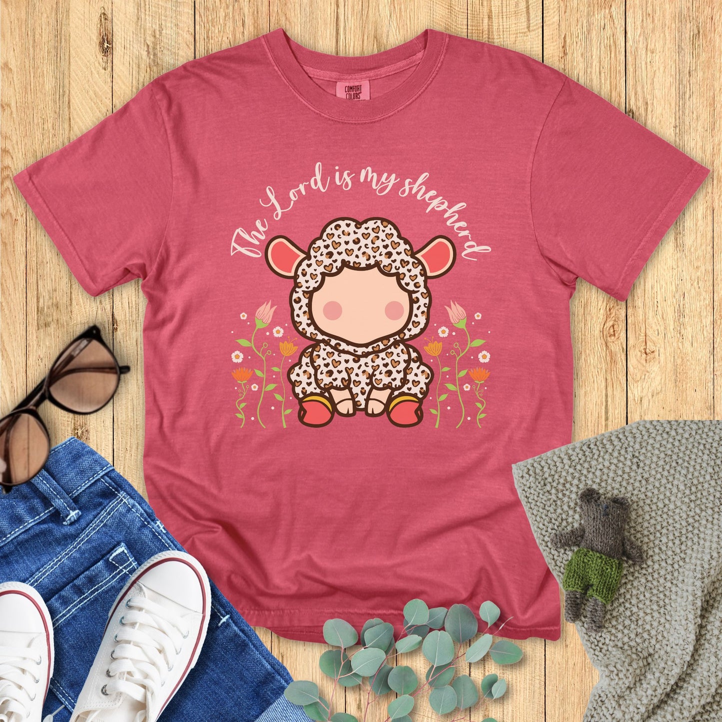 crimson red t-shirt with a cartoon lamb design and 'The Lord is my shepherd' text on a wooden surface.