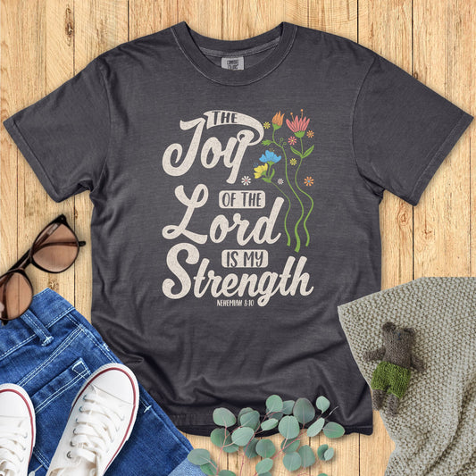 Dark gray t-shirt with 'The Joy of the Lord is My Strength' text on a wooden surface with accessories.