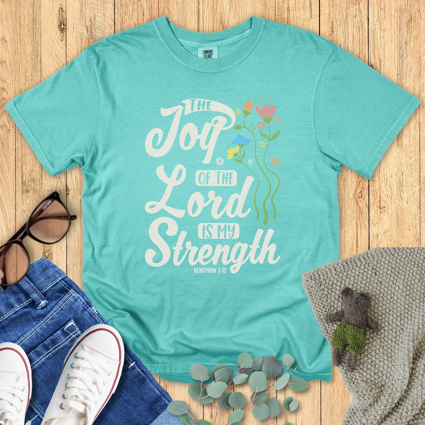 Turquoise t-shirt with motivational quote on a wooden surface with accessories.
