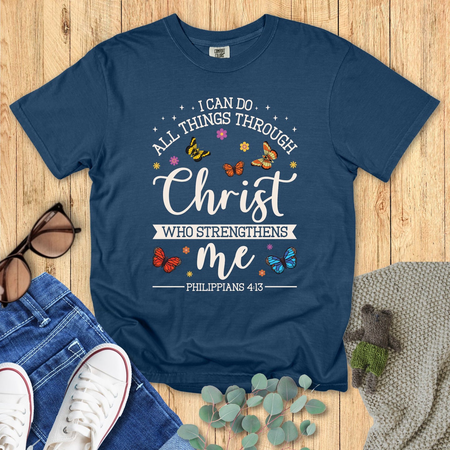 Blue t-shirt with motivational quote on a wooden surface with accessories.