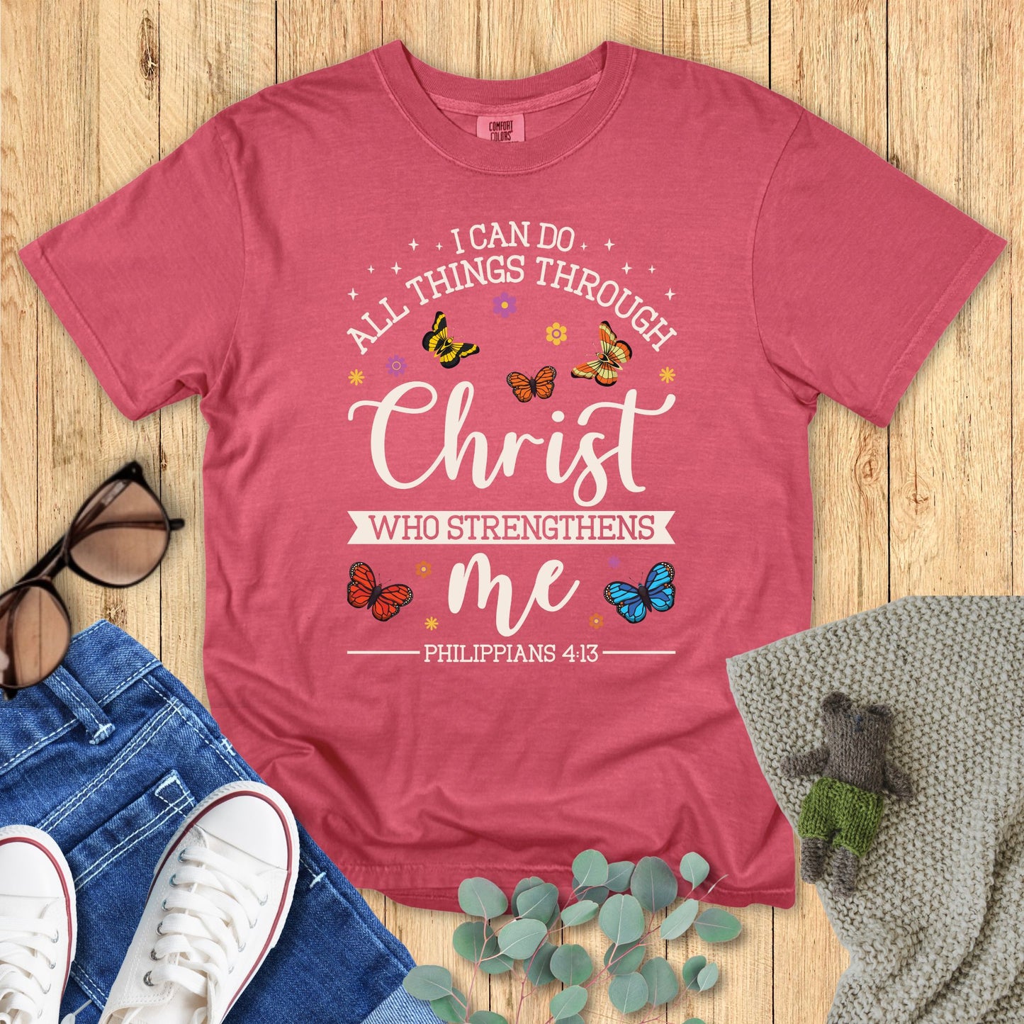 red t-shirt with motivational quote on a wooden surface with accessories.