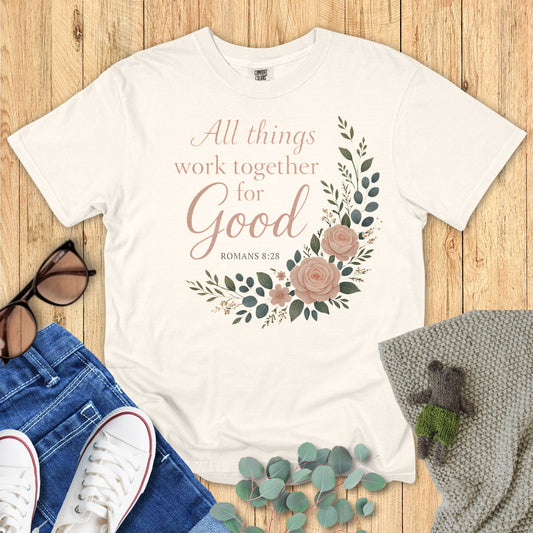 Ivory t-shirt with floral design and text on a wooden surface with accessories.
