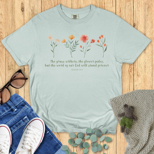 Light blue t-shirt with floral design and text on a wooden surface with accessories.