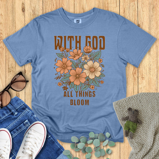Blue t-shirt with floral design and text on a wooden surface with accessories.