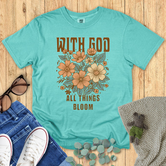 Teal t-shirt with floral design and text on a wooden surface with accessories.