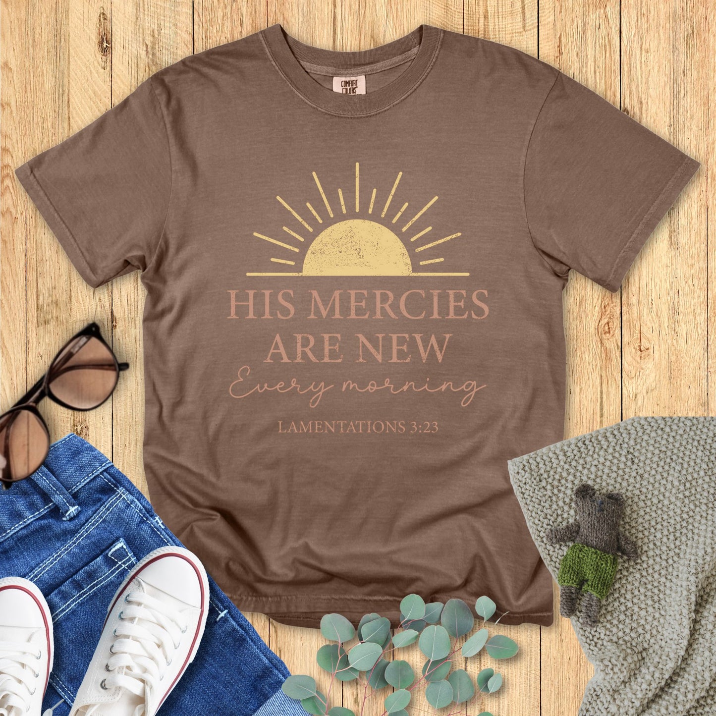 Brown t-shirt with motivational quote on a wooden surface with accessories.