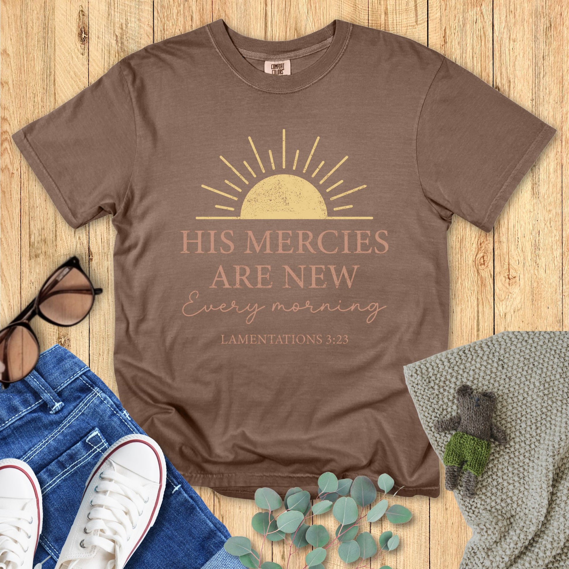 Brown t-shirt with motivational quote on a wooden surface with accessories.