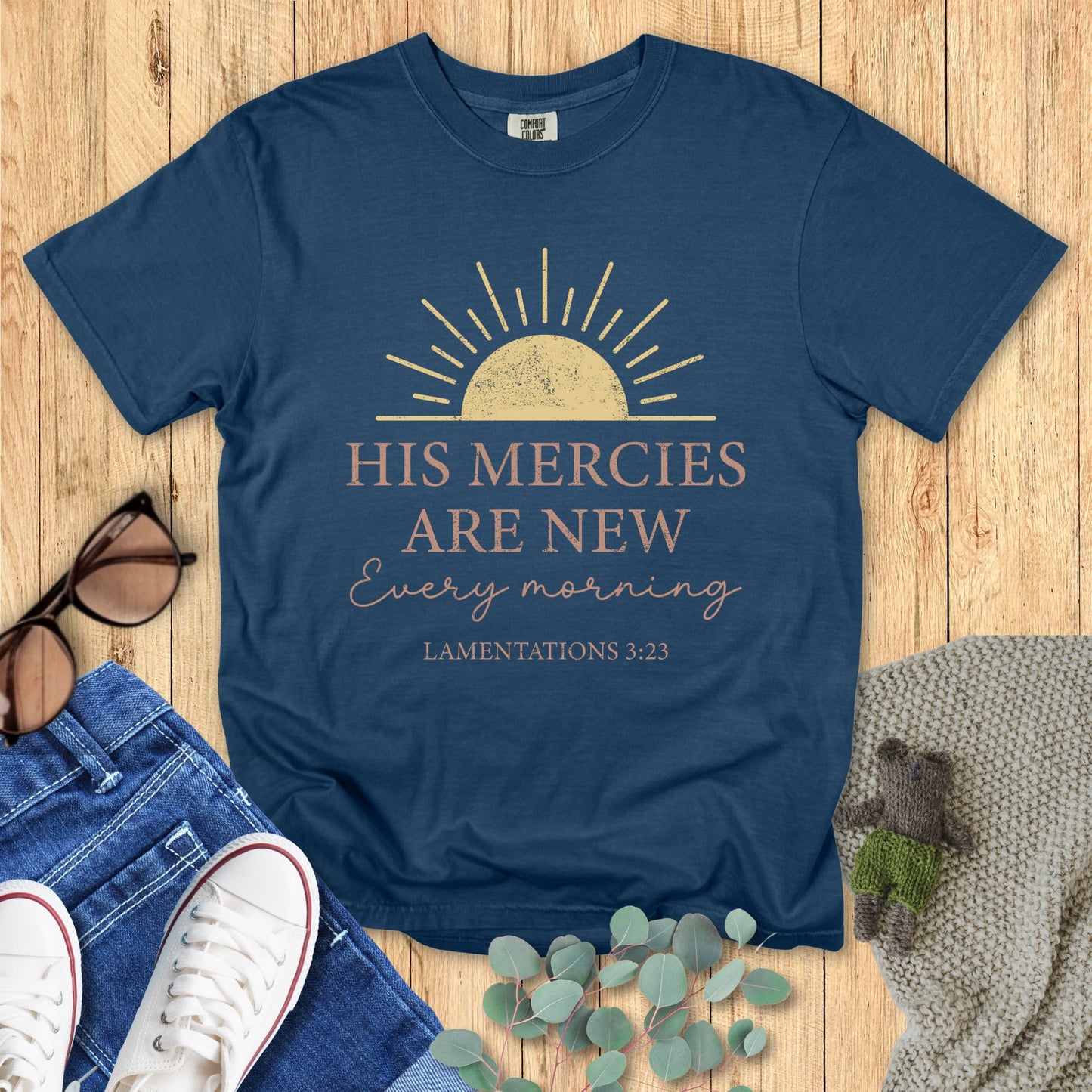 Blue t-shirt with motivational quote on a wooden surface with accessories.