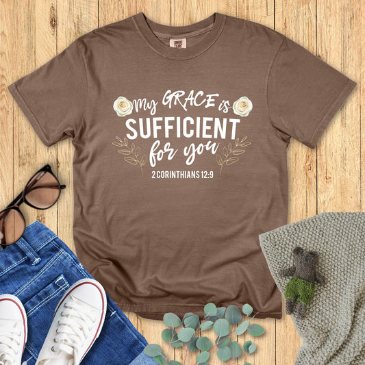 Brown t-shirt with 'My grace is sufficient for you' text on a wooden surface with accessories.