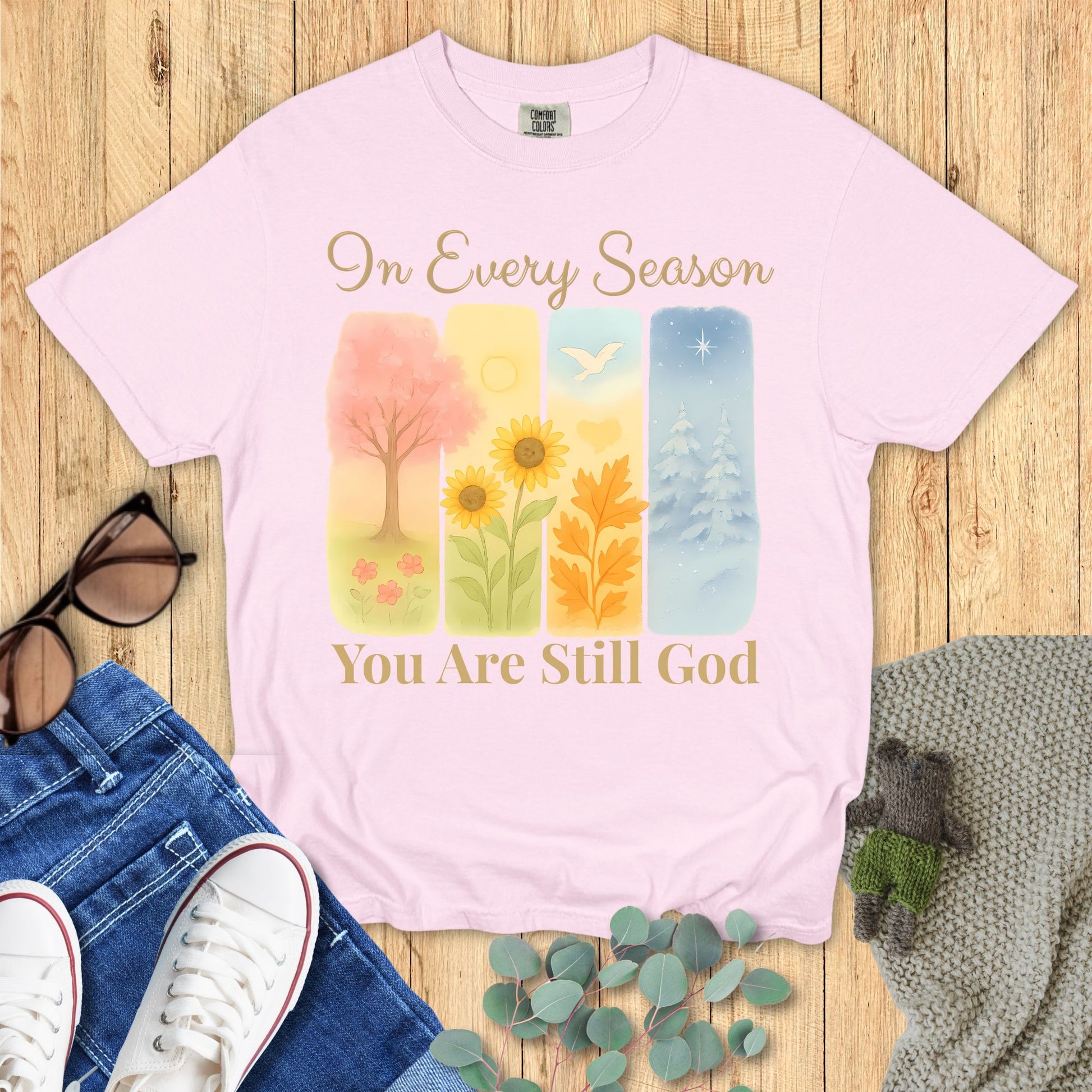 Pink t-shirt with artistic design and text on a wooden surface with accessories.