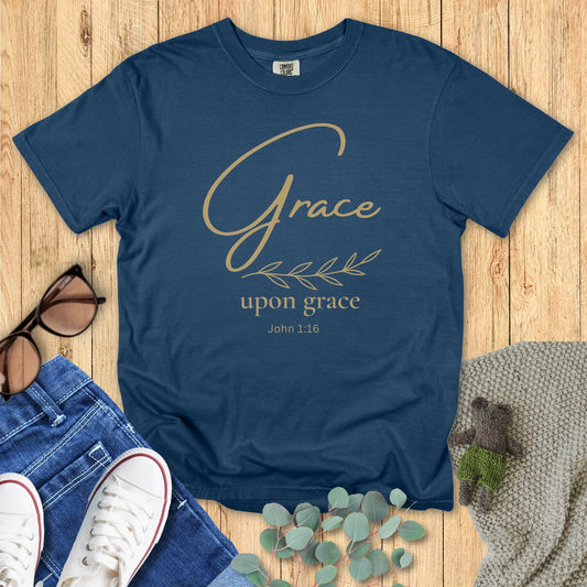 Navy Christian T-shirt with gold script reading “Grace Upon Grace” and John 1:16, accented by a minimalist olive branch illustration.