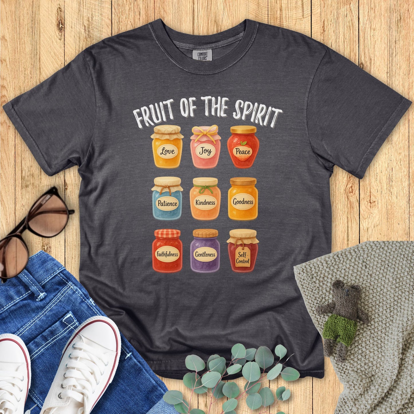 Dark gray t-shirt with 'Fruit of the Spirit' design on a wooden surface with accessories.