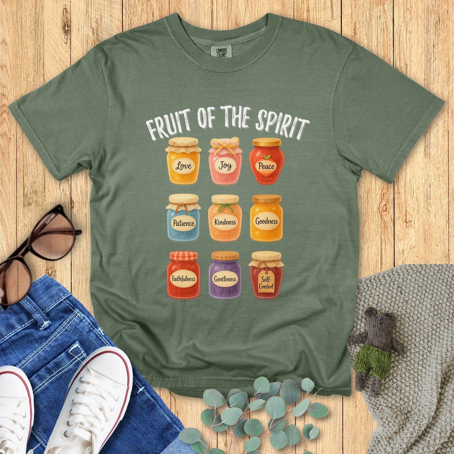 Green t-shirt with 'Fruit of the Spirit' design on a wooden surface with accessories.
