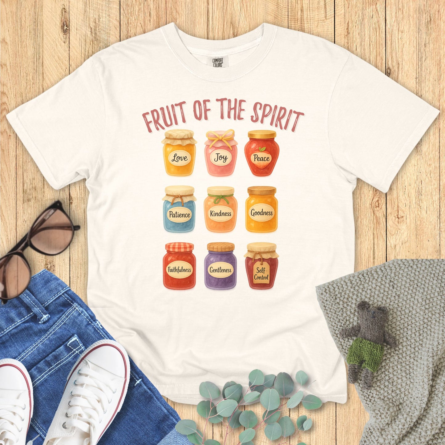 Ivory t-shirt with 'Fruit of the Spirit' design on a wooden surface with accessories.