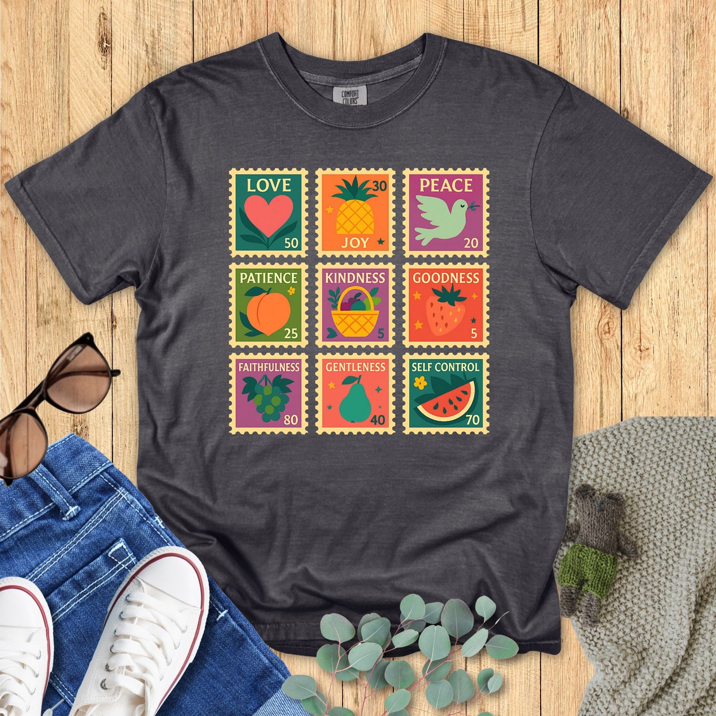Dark gray t-shirt with colorful graphic design on a wooden surface with jeans and sneakers.