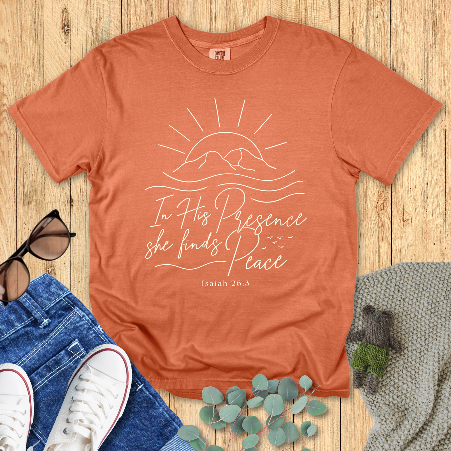 Orange t-shirt with motivational quote on a wooden surface with accessories.