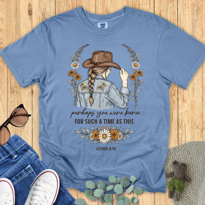 Blue t-shirt with a graphic design of a woman wearing a hat, surrounded by flowers, on a wooden surface.