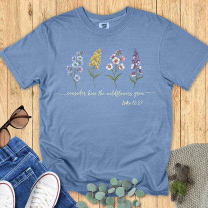 Comfort Colors 1717 Christian women t-shirt in blue jean flat lay. Faith-based design shows four wildflower illustrations with the scripture “Consider how the wildflowers grow – Luke 12:27