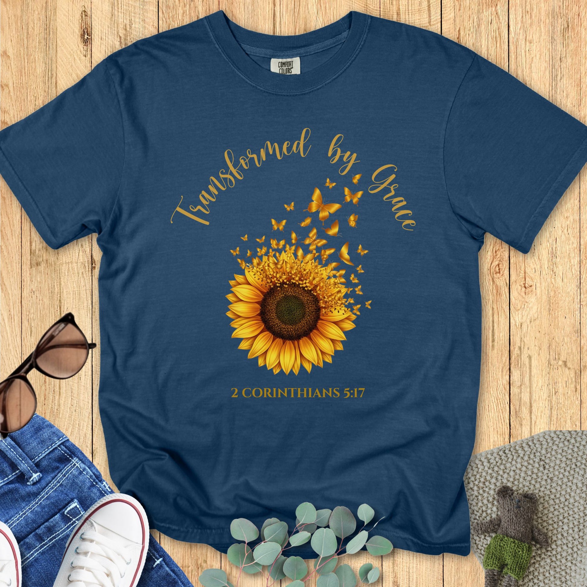 Comfort Colors 1717 Christian women t-shirt in midnight navy flat lay. Faith-based sunflower and butterfly design with the phrase “Transformed by Grace – 2 Corinthians 5:17