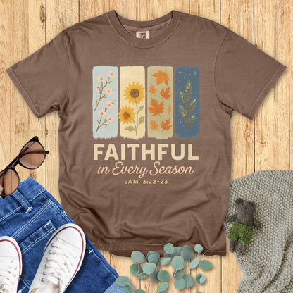 Flat lay of Comfort Colors 1717 Espresso Christian women’s t-shirt. Faith-based design displays “Faithful in Every Season” with scripture reference Lam 3:22-23 under four illustrated seasonal motifs. Styled with cozy accessories and casual props on a rustic wood background