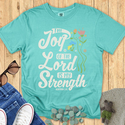 Comfort Colors 1717 Christian women’s t-shirt in seafoam green, laid flat with casual styling props. White distressed lettering and colorful floral accents display the verse “The Joy of the Lord is My Strength – Nehemiah 8:10