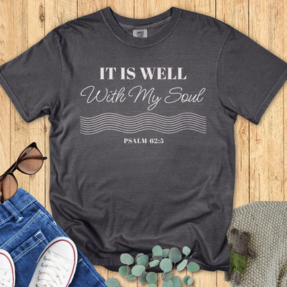 Christian women’s t-shirt on Comfort Colors 1717 in pepper gray with the phrase ‘It Is Well With My Soul – Psalm 62:5’ in white script and serif font, styled flat lay with jeans, sneakers, sunglasses, and eucalyptus leaves