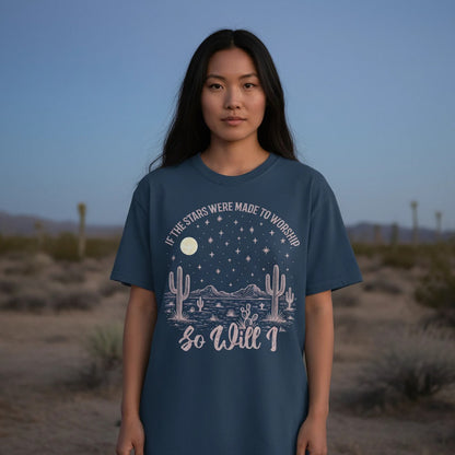 Young woman standing in the desert at dusk wearing a Christian women’s t-shirt that says 'If the stars were made to worship so will I,' featuring moon, stars, mountains, and cactus artwork