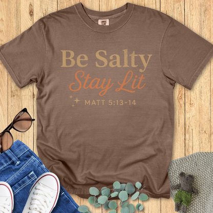 Espresso brown Comfort Colors 1717 shirt with the Christian message “Be Salty Stay Lit – Matt 5:13-14,” styled flat lay with casual wear