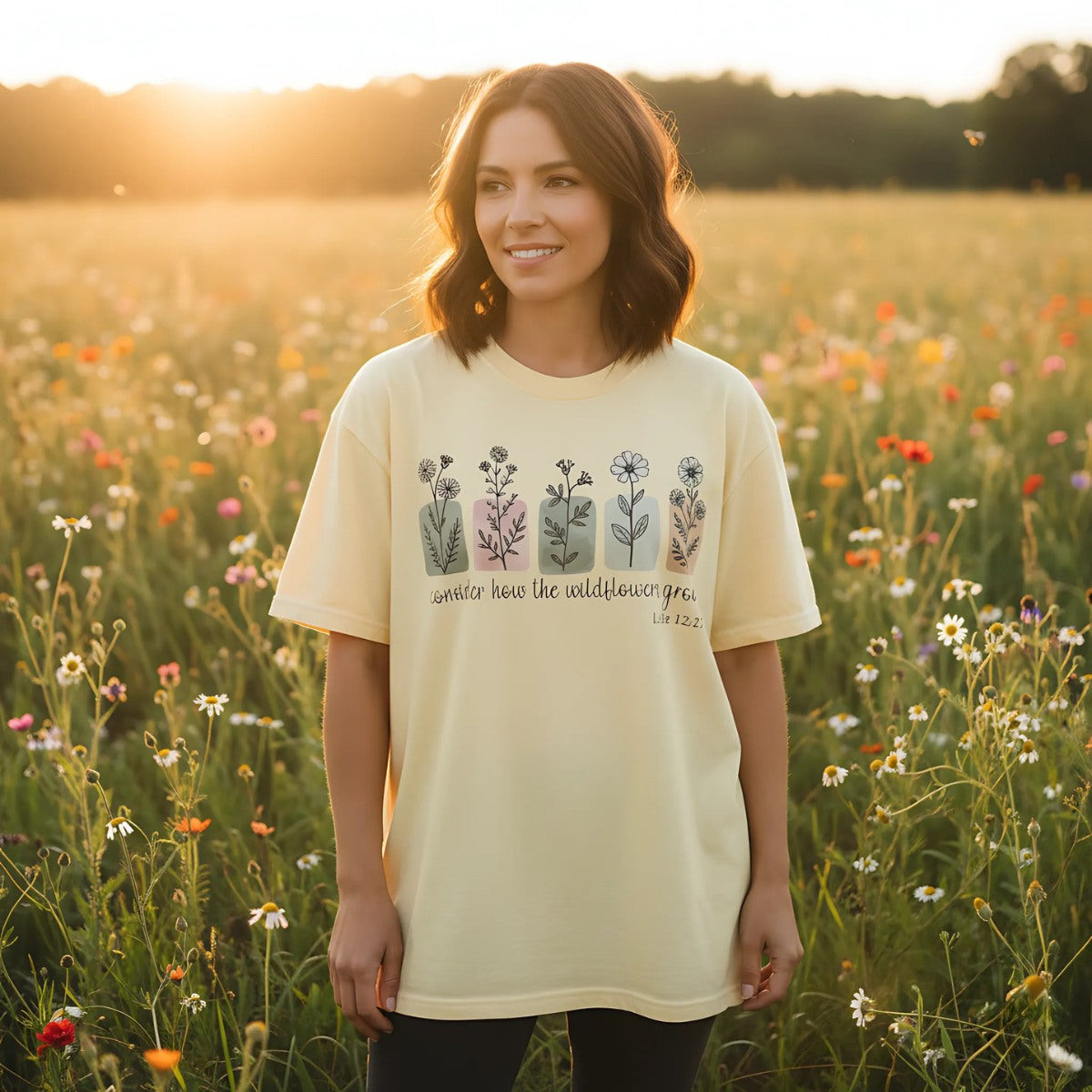 Lifestyle photo – Woman standing in a sunlit wildflower field wearing butter yellow Comfort Colors 1717 Christian T-shirt with “Consider how the wildflowers grow – Luke 12:27” design, smiling in nature.