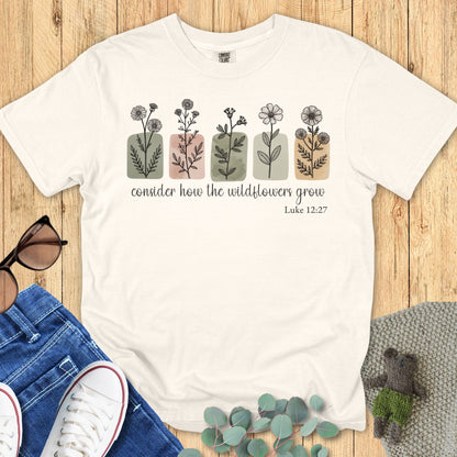 Ivory Comfort Colors 1717 T-shirt mockup – Faith-based shirt in ivory, flat lay with wildflower illustrations and scripture Luke 12:27, styled with casual accessories
