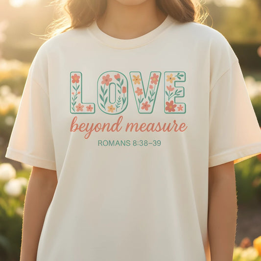 Ivory Comfort Colors Christian T-shirt with floral design spelling "LOVE beyond measure," scripture Romans 8:38–39. Modeled outdoors in a flower garden setting for a soft lifestyle look.